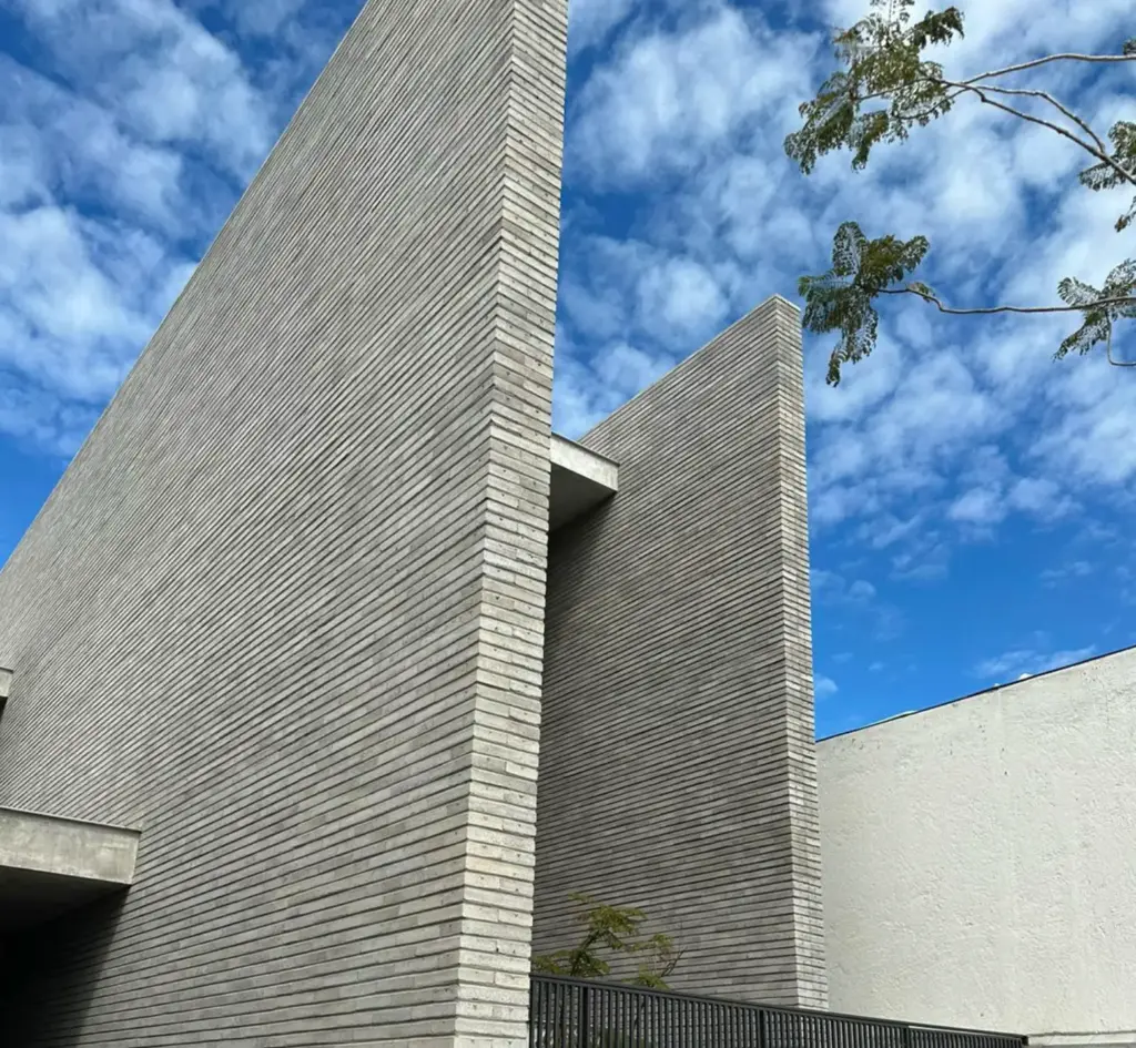 Arquitectura moderna con muros de ladrillo gris bajo un cielo azul nublado.