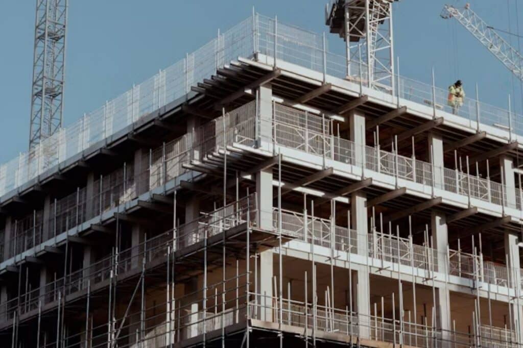 Edificio en construcción con andamios, grúas y obrero con casco amarillo