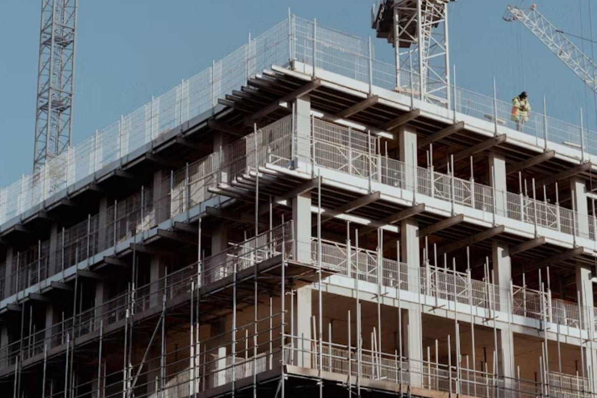 Edificio en construcción con andamios, grúas y obrero con casco amarillo
