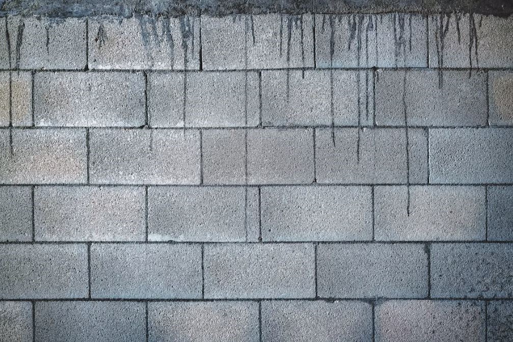 Muro de block de concreto gris con goteos oscuros en la parte superior.